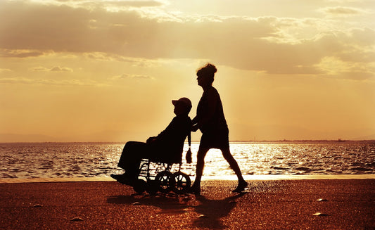 Woman pushing man in wheelchair on sunset beach. Image by Adam from Pixabay